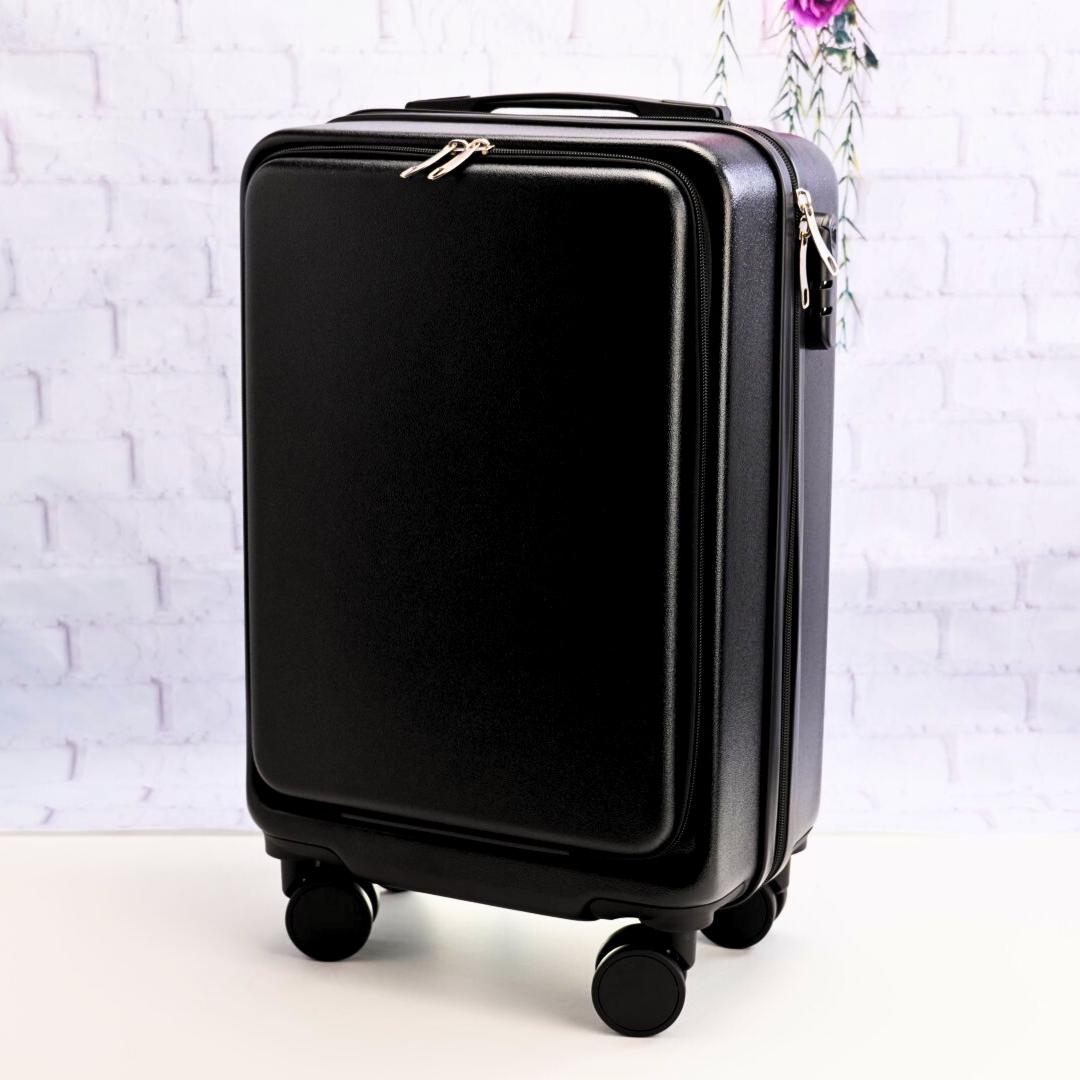 Angled front view of a plain black carry-on suitcase showing the zippered front panel, top handle and spinner wheels