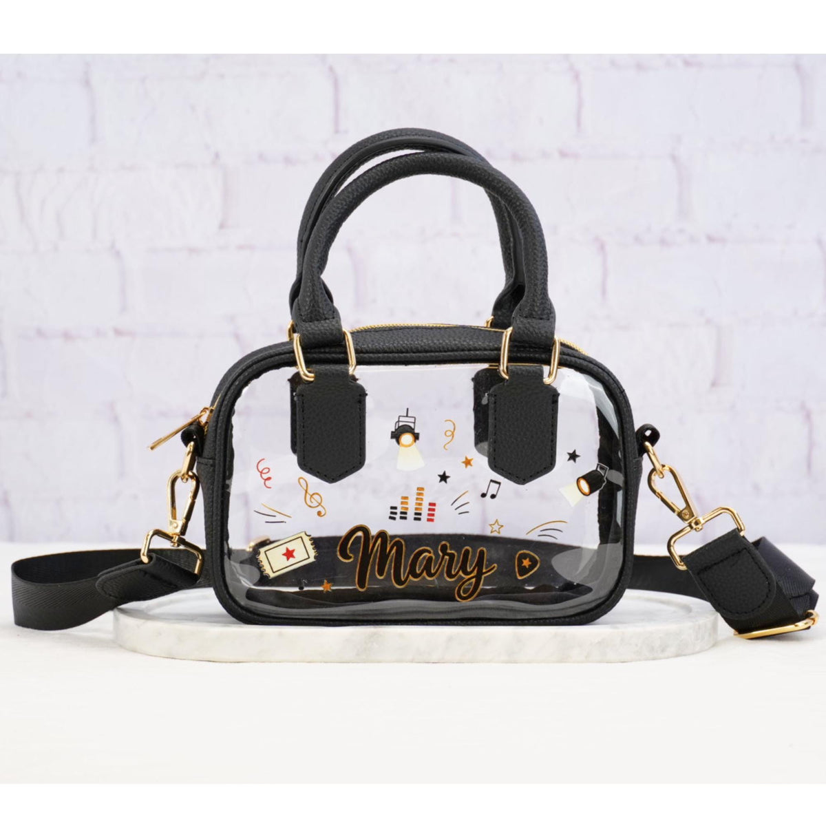 Clear stadium crossbody bag with black trim, shoulder strap and music graphics, personalized with example name Mary