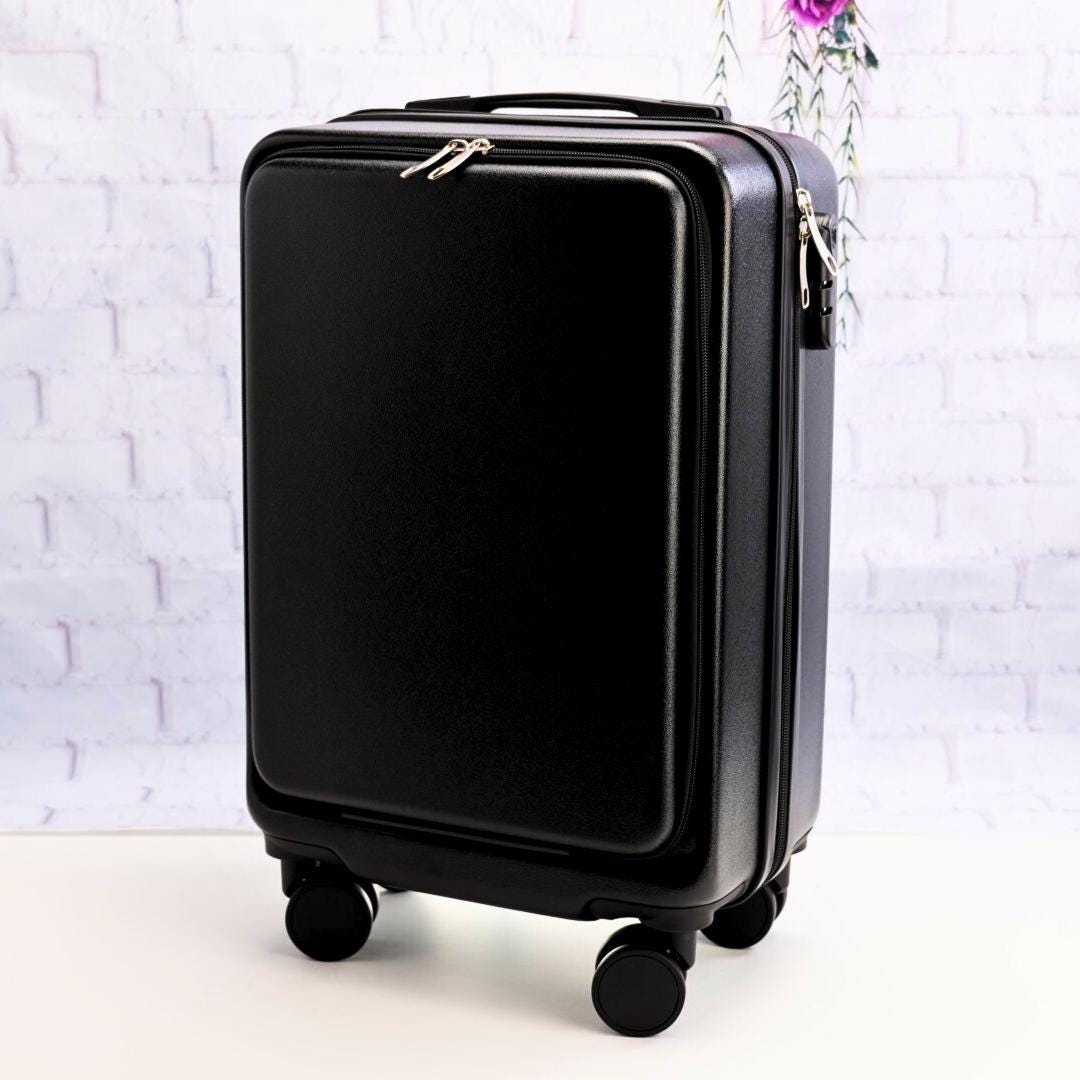 Angled front view of a plain black carry-on suitcase showing the zippered front panel, top handle and spinner wheels