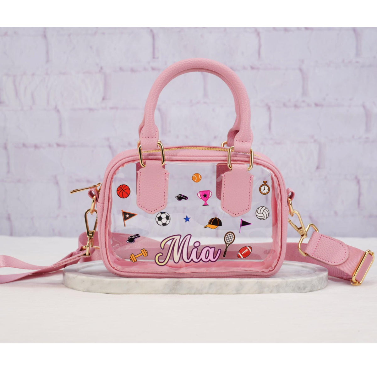 Clear stadium crossbody bag with pink trim, matching strap and sports icons, personalized with example name Mia