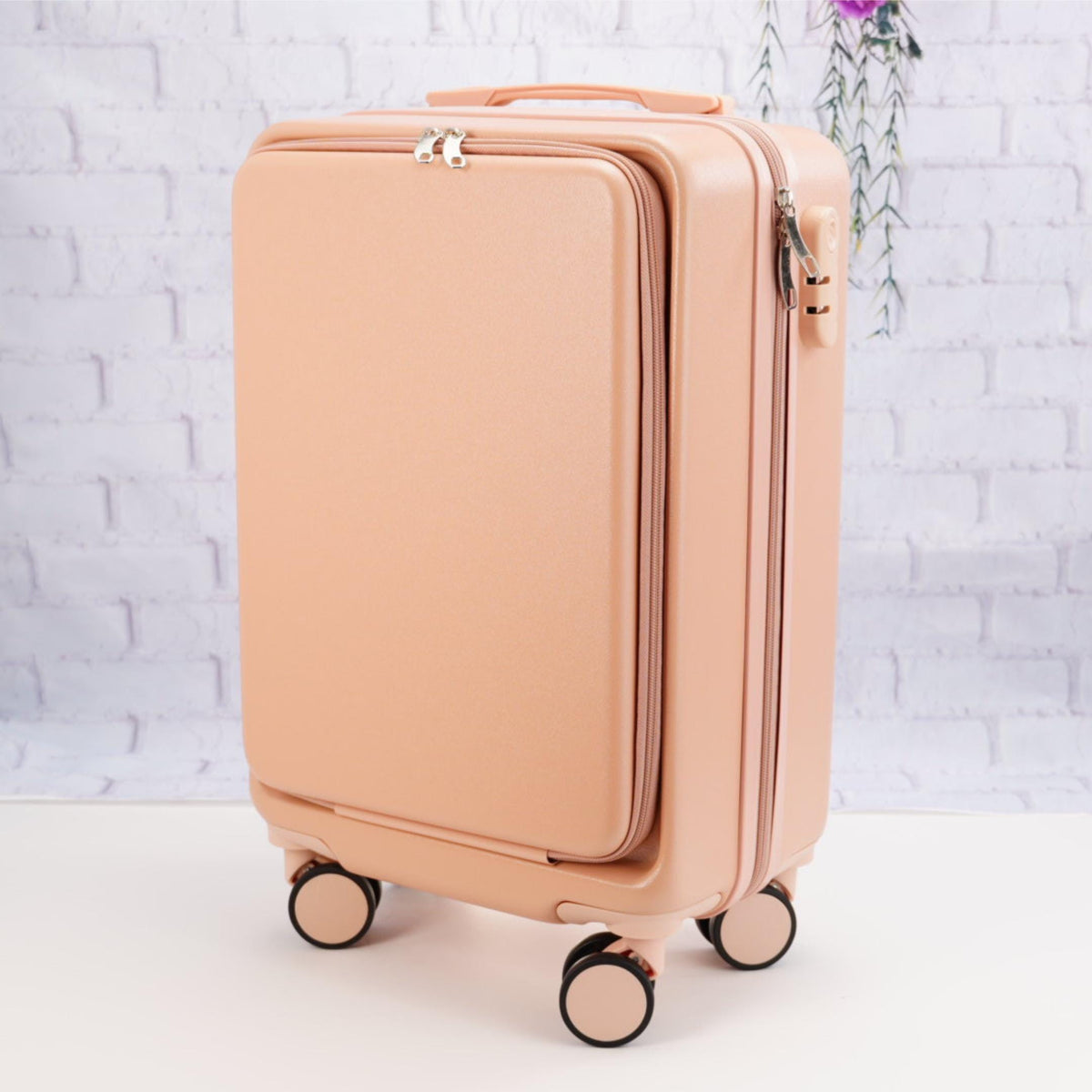 Angled front view of a plain pale pink carry-on suitcase showing the zippered front panel, top handle and spinner wheels