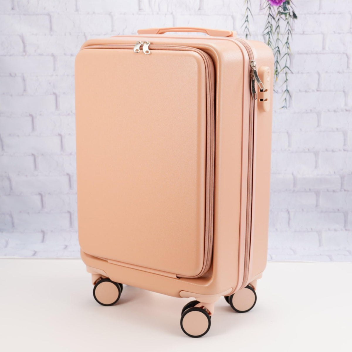 Angled front view of a plain pale pink carry-on suitcase showing the zippered front panel, top handle and spinner wheels